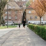 A couple jogging together in an urban park surrounded by greenery and houses.