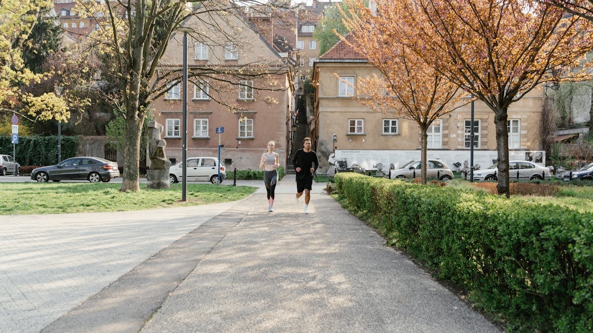 A couple jogging together in an urban park surrounded by greenery and houses.
