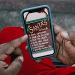 Close-up of hands holding a smartphone displaying Santa's whimsical to-do list outdoors.
